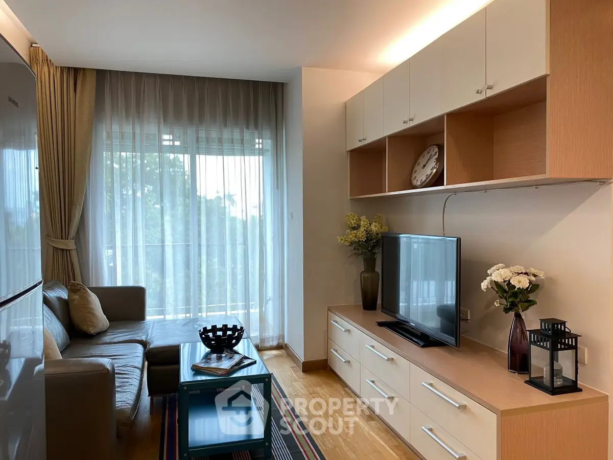 Modern living room with sleek furniture and large window offering natural light and greenery view.