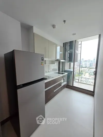 Modern kitchen with sleek cabinets and city view from window, featuring stainless steel fridge and microwave.