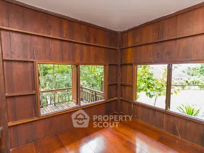 Charming wooden interior with large windows overlooking lush greenery, perfect for a serene living space.