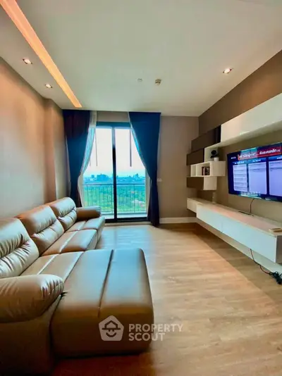 Modern living room with leather sofa and wall-mounted TV, featuring a scenic balcony view.