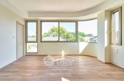Spacious sunlit room with large windows and wooden flooring, perfect for modern living.