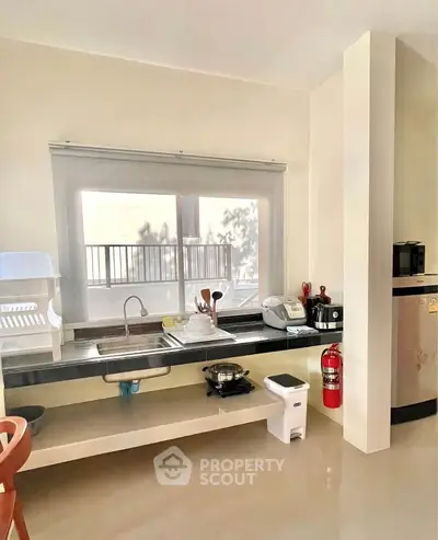 Modern kitchen with sleek countertops and essential appliances, featuring a large window for natural light.