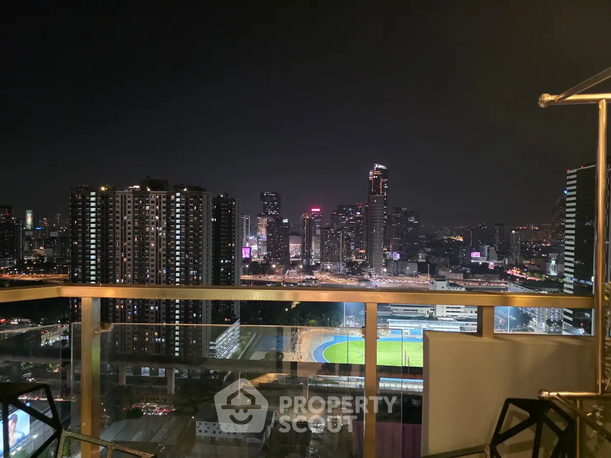 Stunning night cityscape view from a high-rise balcony overlooking urban skyline and sports field.