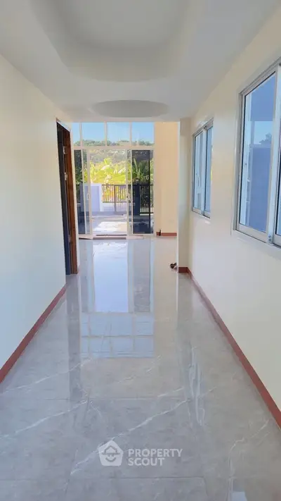 Bright hallway with glossy marble flooring leading to a balcony with scenic views.