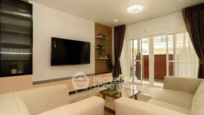 Elegant living room with modern decor and large TV, featuring natural light from glass doors.