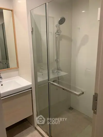Modern bathroom with glass shower enclosure and sleek vanity in contemporary apartment.