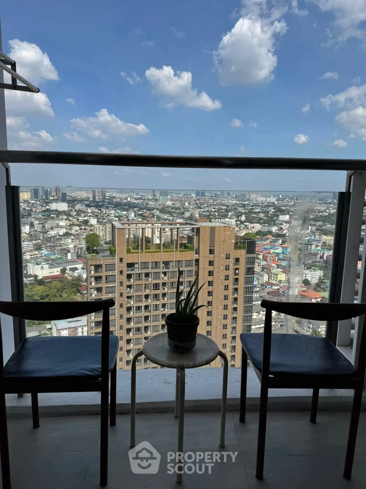 Stunning city view from a high-rise balcony with seating area, perfect for relaxation.