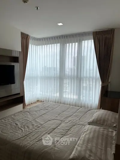 Spacious bedroom with large windows and modern decor in a high-rise apartment.