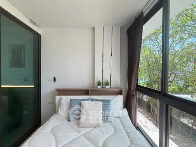 Bright bedroom with large windows and lush greenery view, featuring modern decor and cozy bedding.