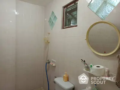 Cozy bathroom with tiled walls and round mirror, featuring a shower and essential toiletries.