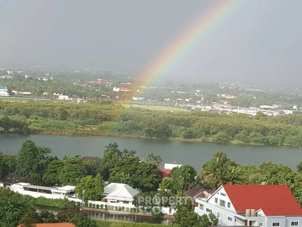Stunning aerial view of lush greenery and river with vibrant rainbow over residential area.
