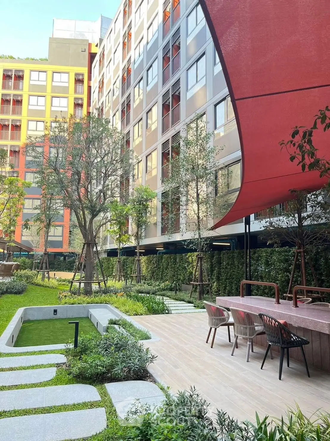 Modern apartment building with lush garden and outdoor seating area.
