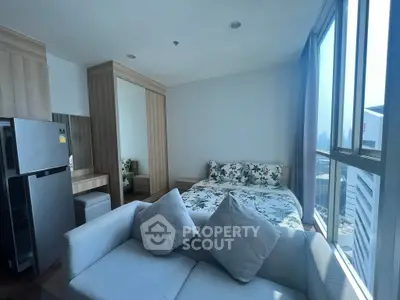 Modern studio apartment with large windows and city view, featuring a cozy bed and compact kitchen area.