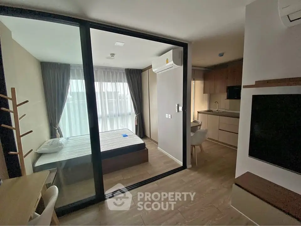 Modern studio apartment with glass partition, cozy bedroom, and compact kitchen.