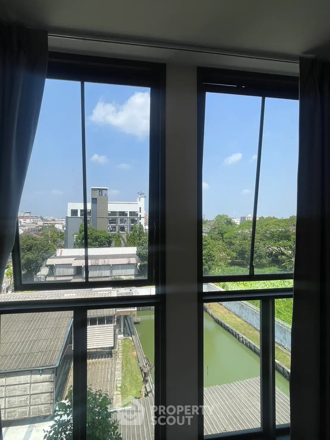 Stunning urban view from modern apartment window with lush greenery and blue sky.