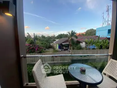 Charming balcony with outdoor seating offering a serene view of lush greenery and distant houses.
