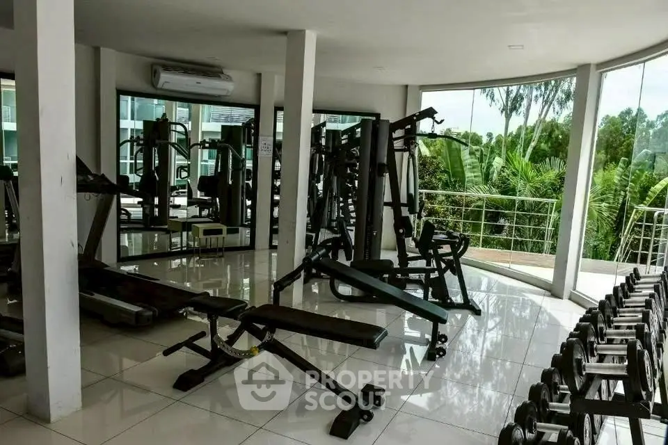 Spacious gym with modern equipment and lush greenery view, perfect for fitness enthusiasts.