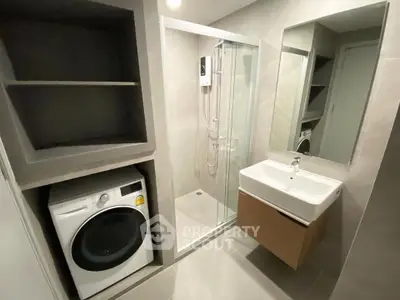 Modern bathroom with shower, washing machine, and sleek sink in a stylish apartment.