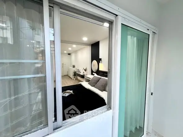 Modern bedroom view through sliding glass window with sleek interior design and cozy ambiance.