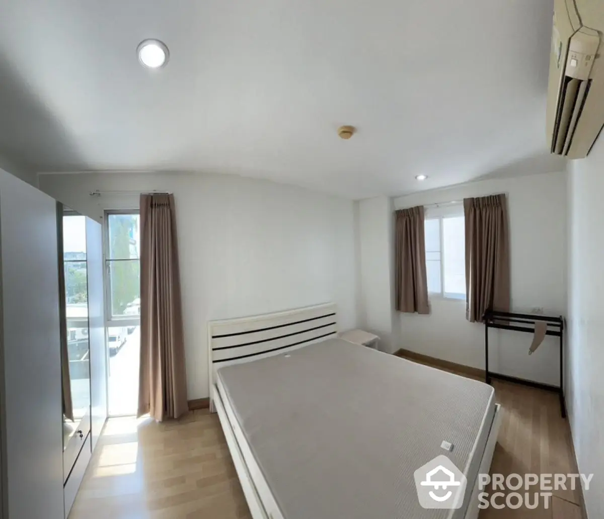 Spacious bedroom with large windows and modern furnishings in a bright apartment.