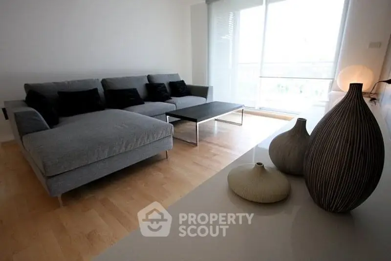 Modern living room with stylish gray sofa and decorative vases, featuring natural light from large windows.