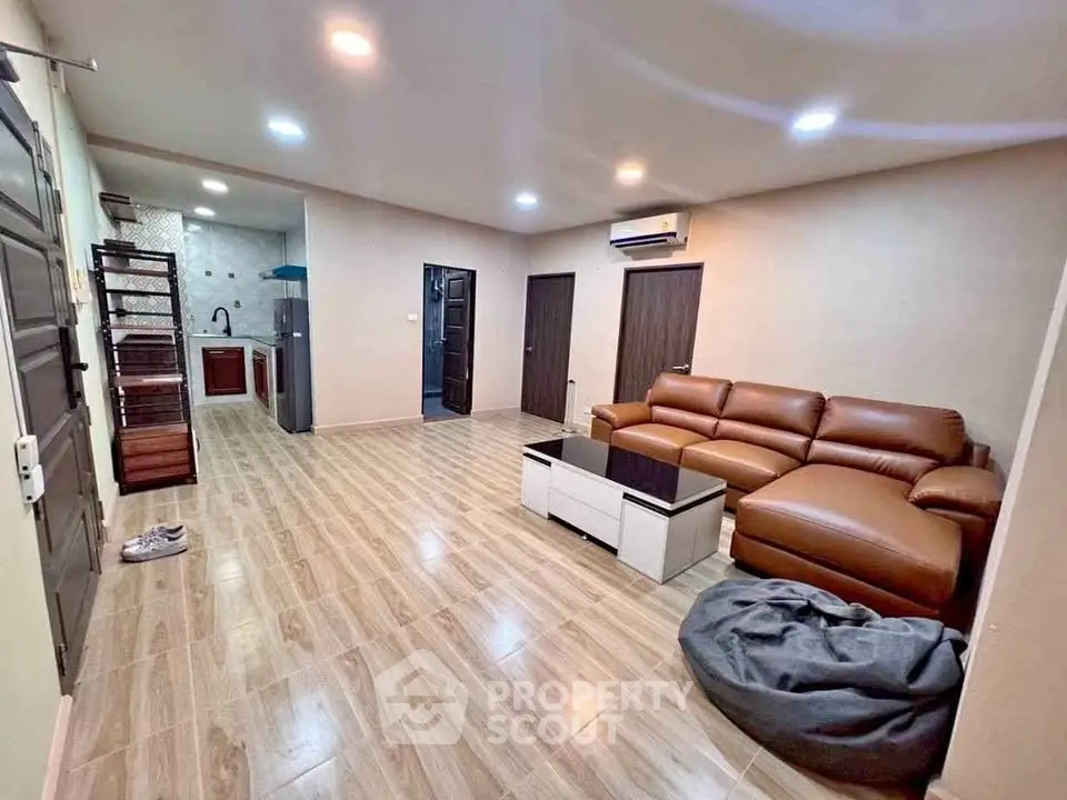 Spacious living room with modern leather sofa and open kitchen layout, perfect for contemporary living.