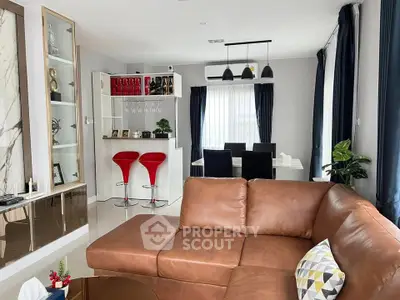 Stylish living room with modern decor and open dining area, featuring a cozy brown leather sofa.