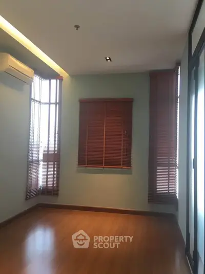 Spacious room with wooden flooring and large windows, perfect for a cozy living space.
