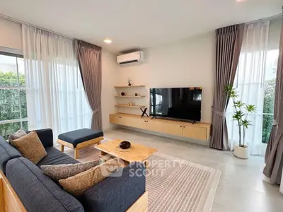 Modern living room with stylish furniture and large TV, featuring natural light and elegant decor.