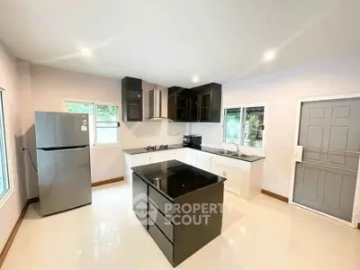 Modern kitchen with sleek island, stainless steel fridge, and gas stove in bright open layout.