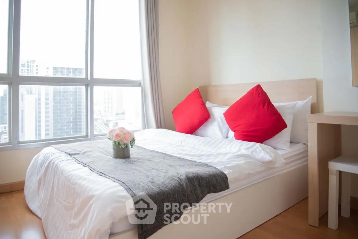 Cozy bedroom with city view, featuring modern decor and vibrant red accents.