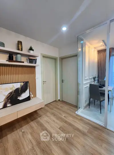 Modern living room with wooden flooring and glass partition leading to dining area.