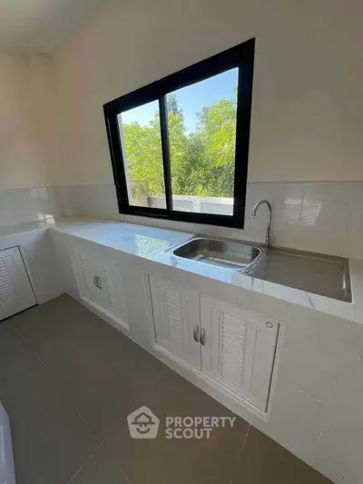 Modern kitchen with sleek countertops and large window offering natural light and greenery view.