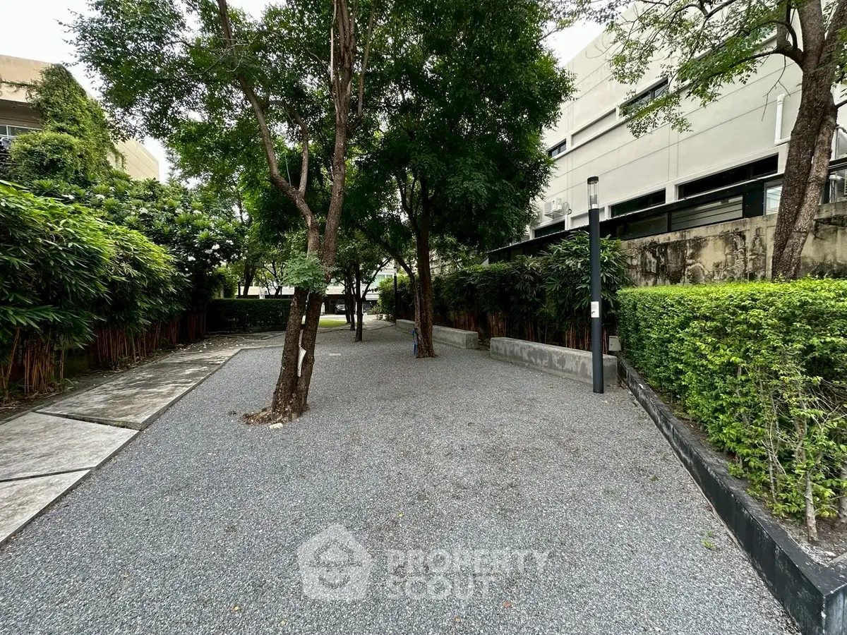 Serene garden area with lush greenery and gravel pathway in modern residential complex.