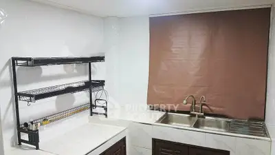 Modern kitchen with sleek white countertops and dual sink, featuring a practical wall-mounted rack.