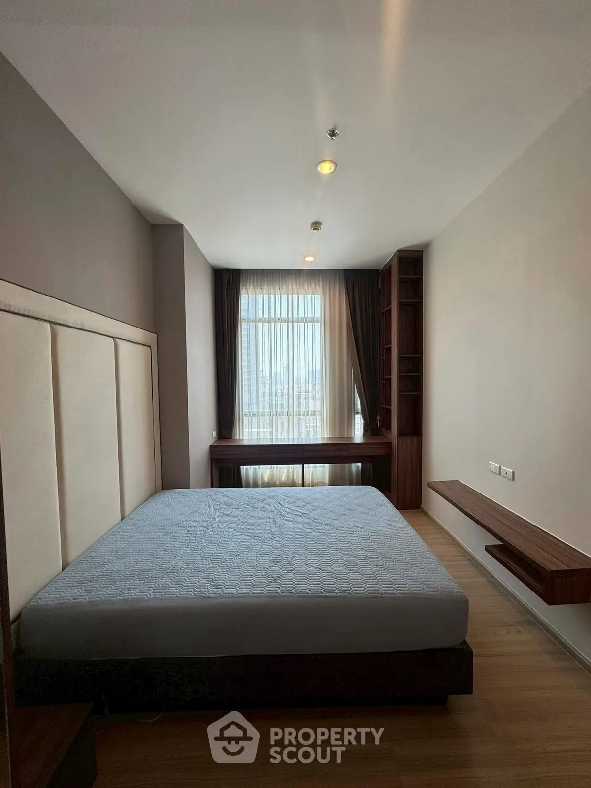 Spacious bedroom with large window and modern furnishings in a high-rise apartment.