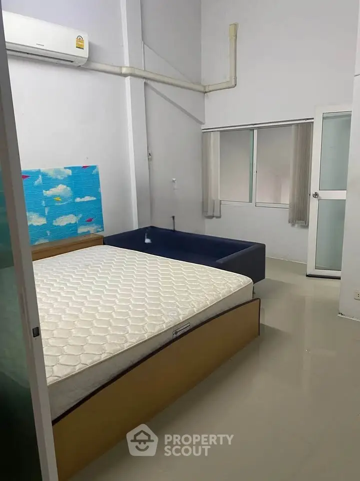 Spacious bedroom with modern design and natural light, featuring a comfortable bed and air conditioning.