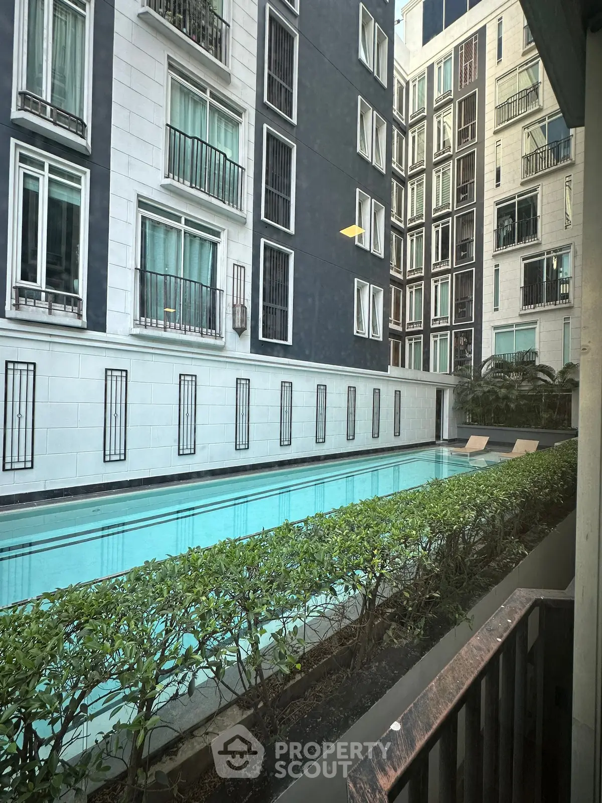 Modern apartment complex with a sleek swimming pool and lush greenery view.