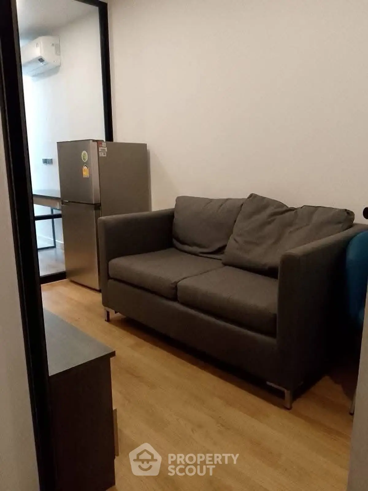 Cozy small living room with a gray sofa and compact fridge, ideal for modern apartments.