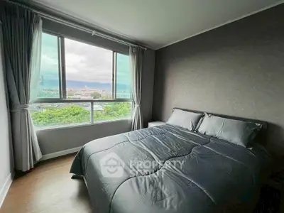 Cozy bedroom with large window offering stunning cityscape views, perfect for relaxation and comfort.
