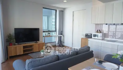 Modern living room with open kitchen, featuring sleek furniture and large window with city view.