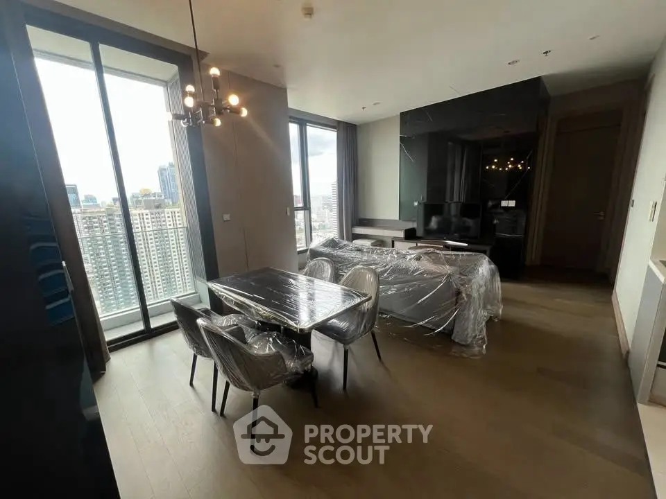 Modern living room with dining area and city view, featuring sleek furniture and large windows.