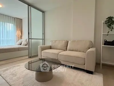 Modern living room with cozy beige sofa and glass coffee table, adjacent to a stylish bedroom.