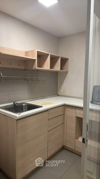 Compact kitchen with light wood cabinets and stainless steel sink in modern apartment.