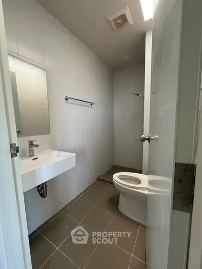 Modern bathroom with sleek fixtures and minimalist design, featuring a toilet, sink, and shower area.