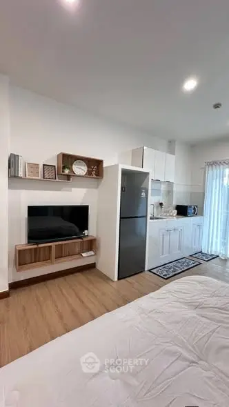 Modern studio apartment with open kitchen and cozy living area, featuring a sleek fridge and stylish decor.
