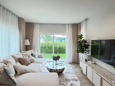 Elegant living room with plush sofa, large TV, and garden view through sliding glass doors.