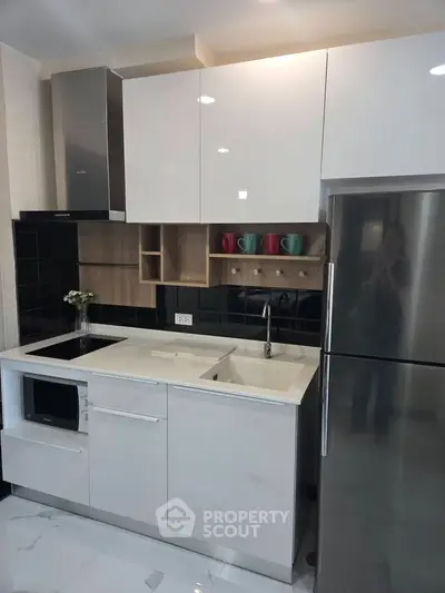 Modern kitchen with sleek white cabinets, stainless steel fridge, and built-in microwave.