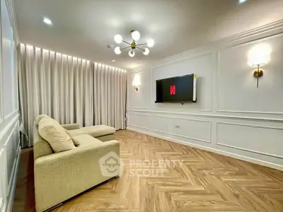 Elegant living room with modern lighting, cozy beige sofa, and wall-mounted TV, featuring stylish herringbone flooring.