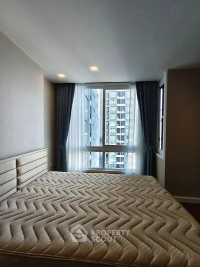 Spacious bedroom with large window offering city view in modern apartment.
